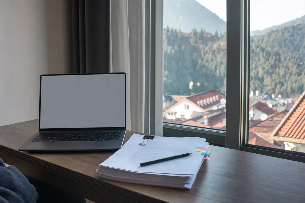 Birou de student cu laptop și lucrare tipărită, lângă o fereastră cu vedere spre munți (imagine generată cu AI)